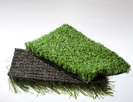 Two small pieces of artificial grass stacked displaying the top and underside.